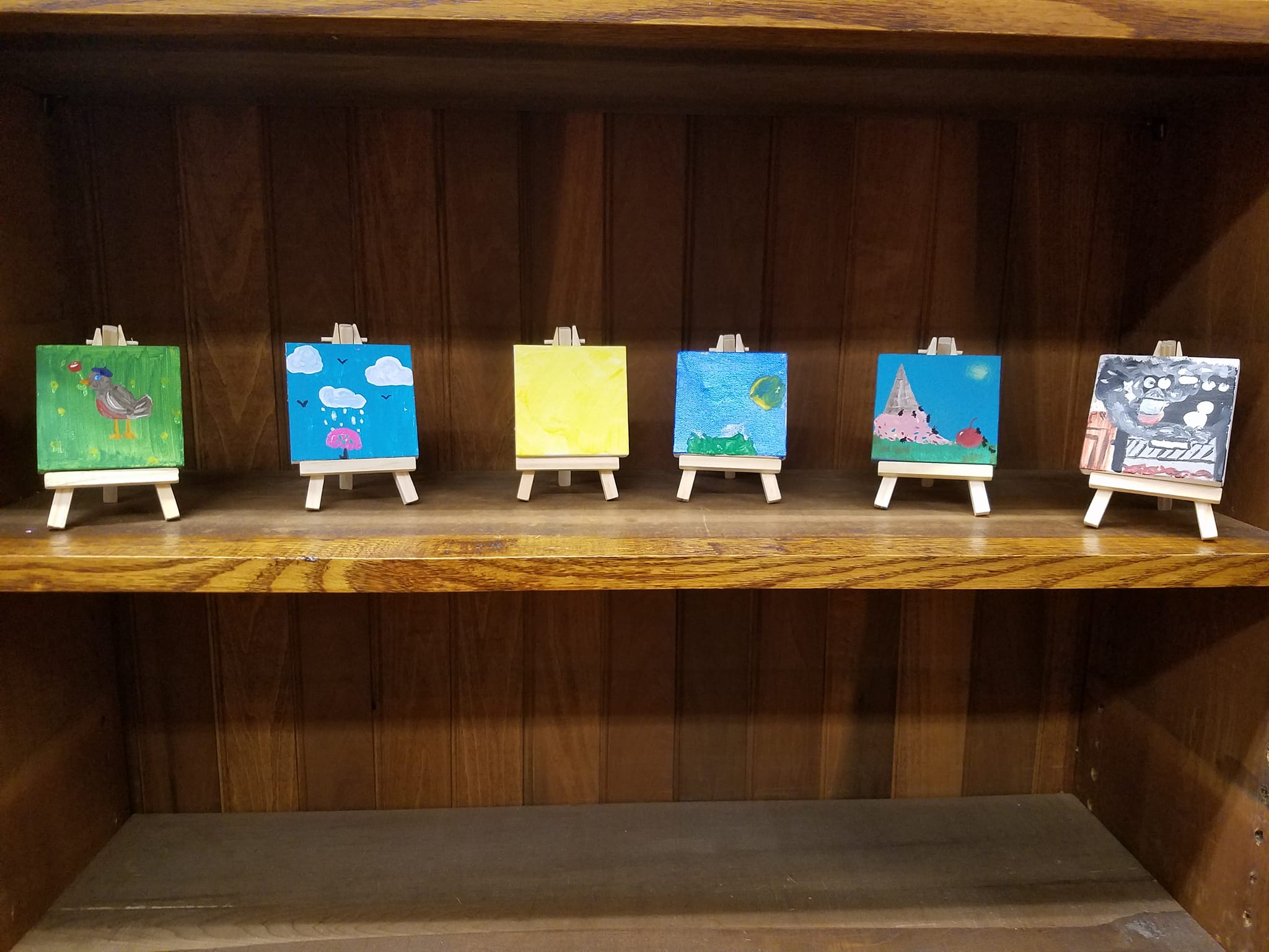 6 painted mini canvases on mini easels displayed on a book shelf